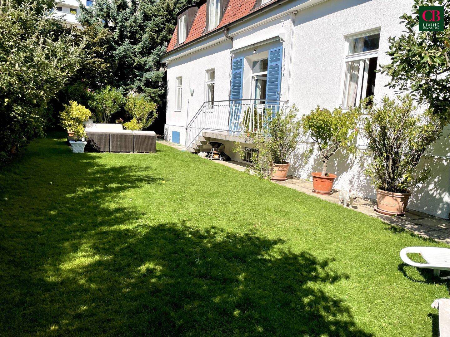 Sonniger Gartenbereich mit Rasenfläche und Outdoor-Sitzgelegenheiten neben der Hausfassade.