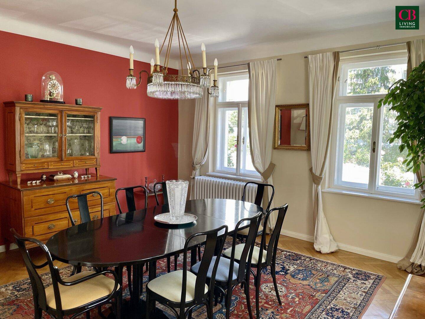 Repräsentatives Esszimmer mit roter Akzentwand, Kronleuchter und klassischem Fischgrätparkett.