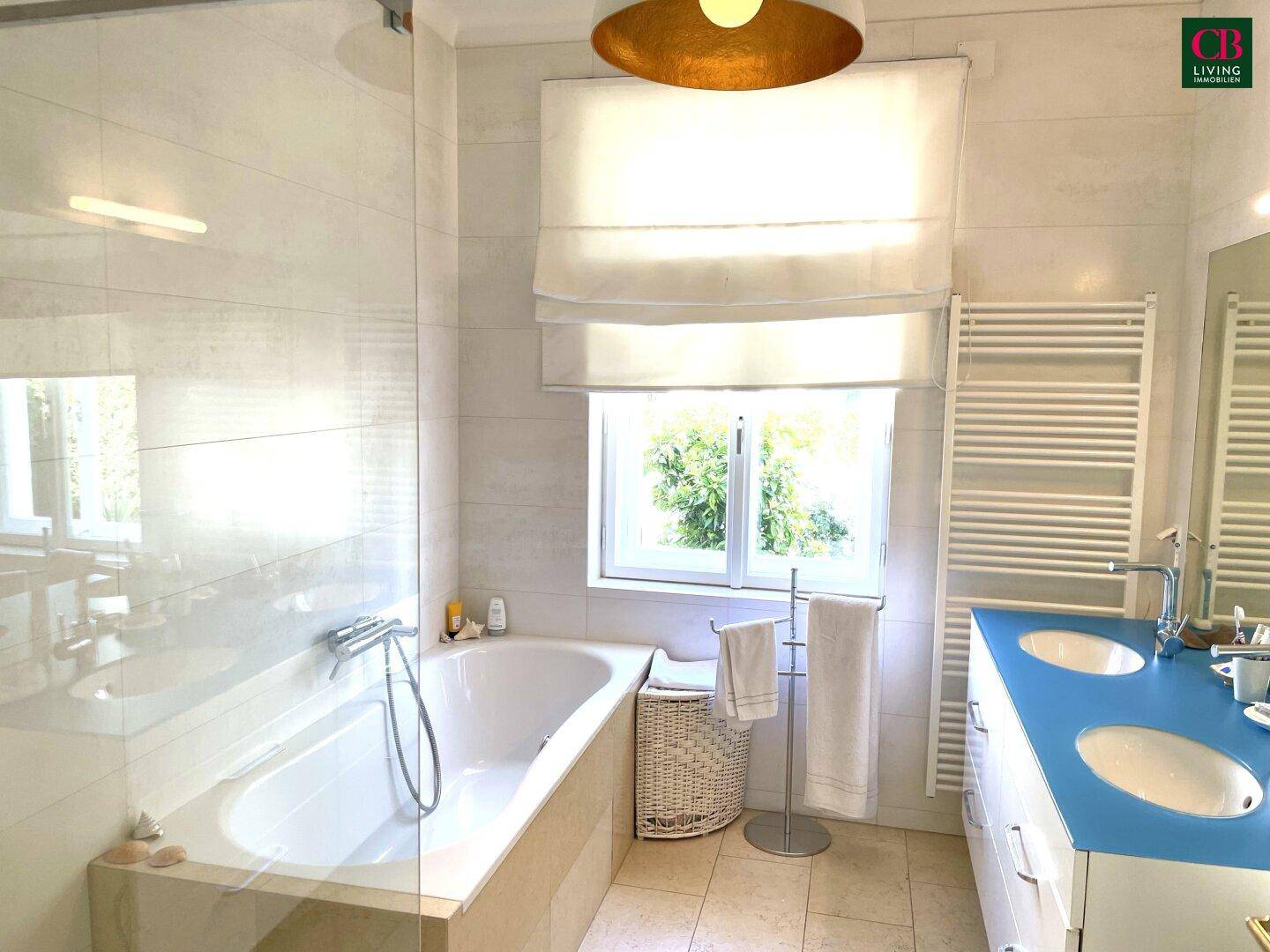 Modernes Badezimmer mit Badewanne, Doppelwaschbecken und großem Fenster für viel Tageslicht.