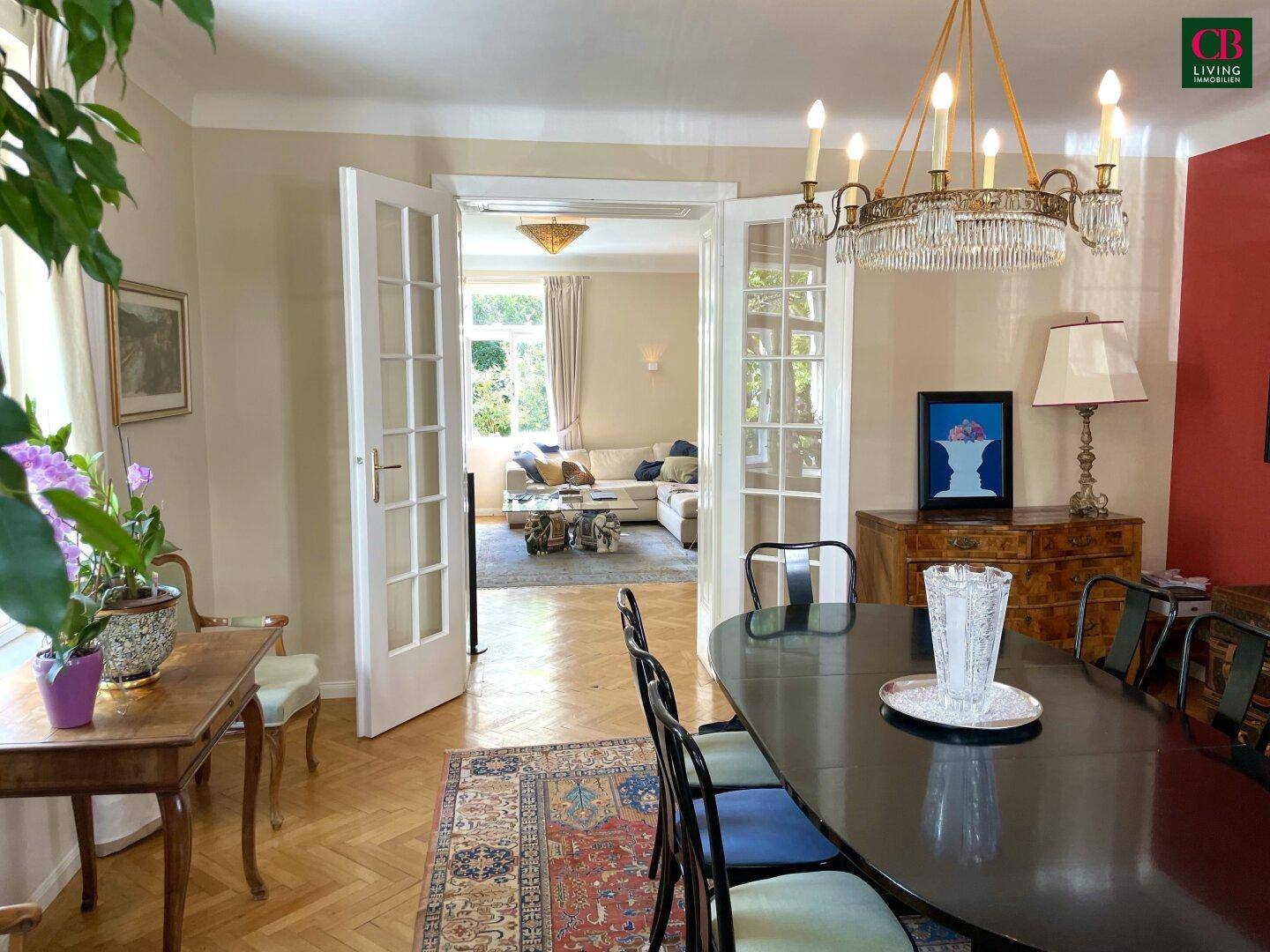 Elegantes Esszimmer mit Parkettboden und Doppeltüren, die zum hellen Wohnzimmer führen.