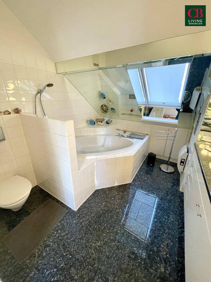 Badezimmer im Dachgeschoss mit Eckbadewanne, Granitboden und Dachfenster für natürliches Licht.