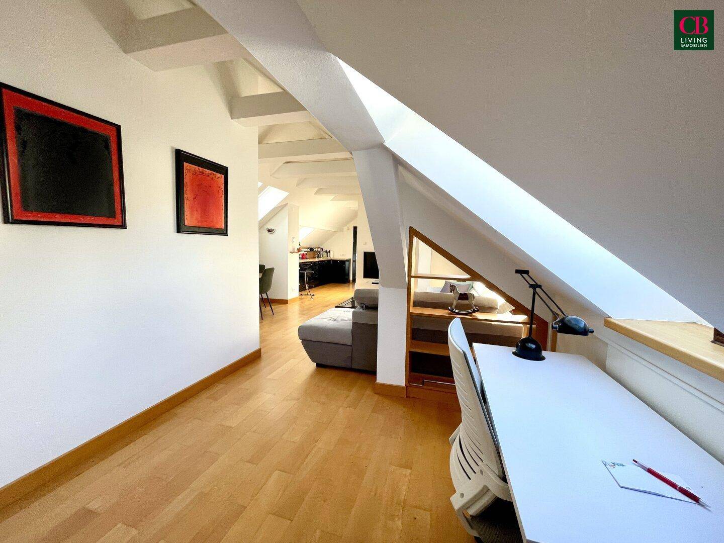 Helles Dachgeschoss-Büro mit Holzboden, Schreibtisch und schrägen Wänden unter dem Dach.