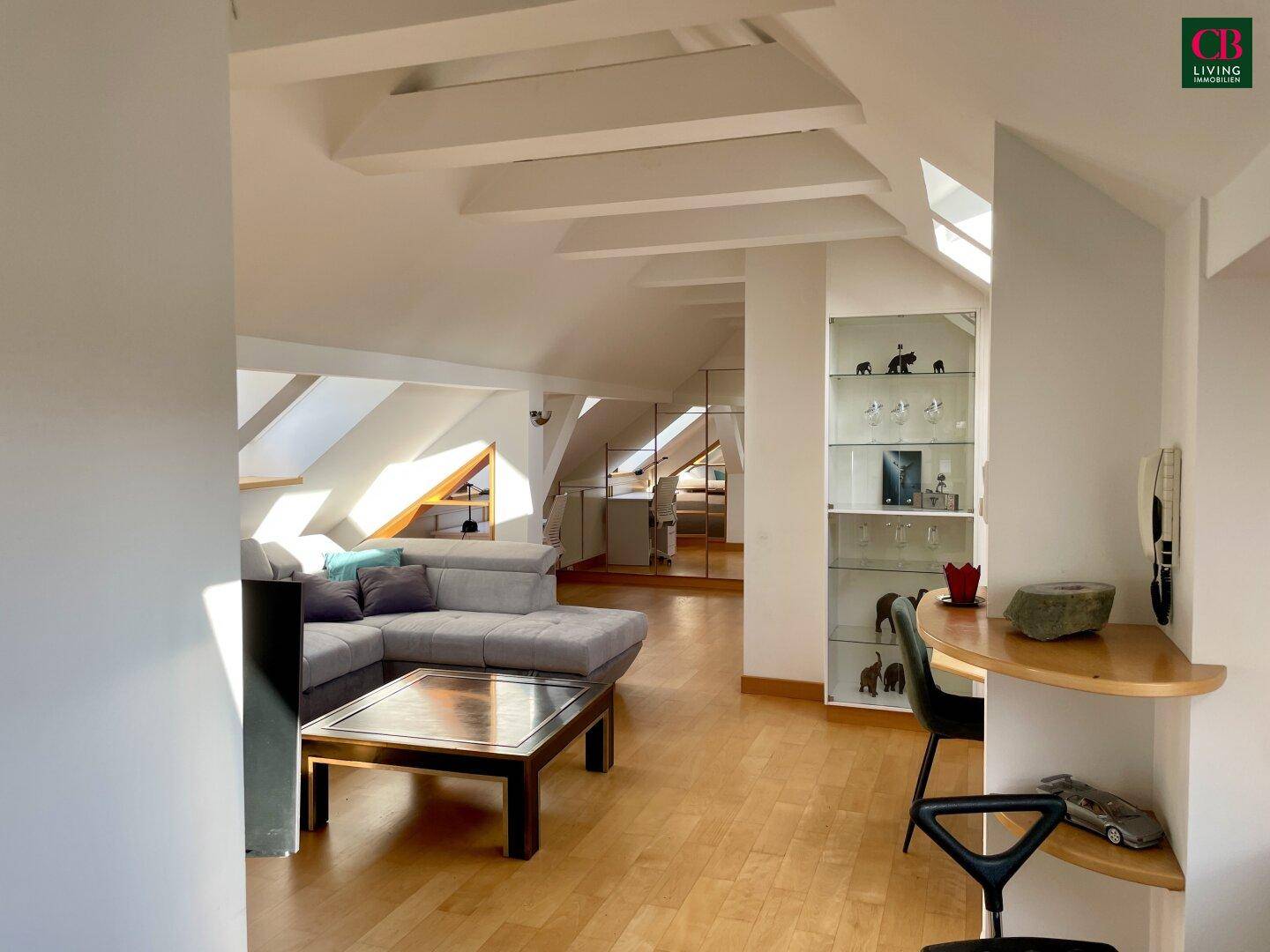 Geräumiger Dachgeschoss-Wohnbereich mit Holzboden, Sofa und integrierten Regalen unter Dachschrägen.