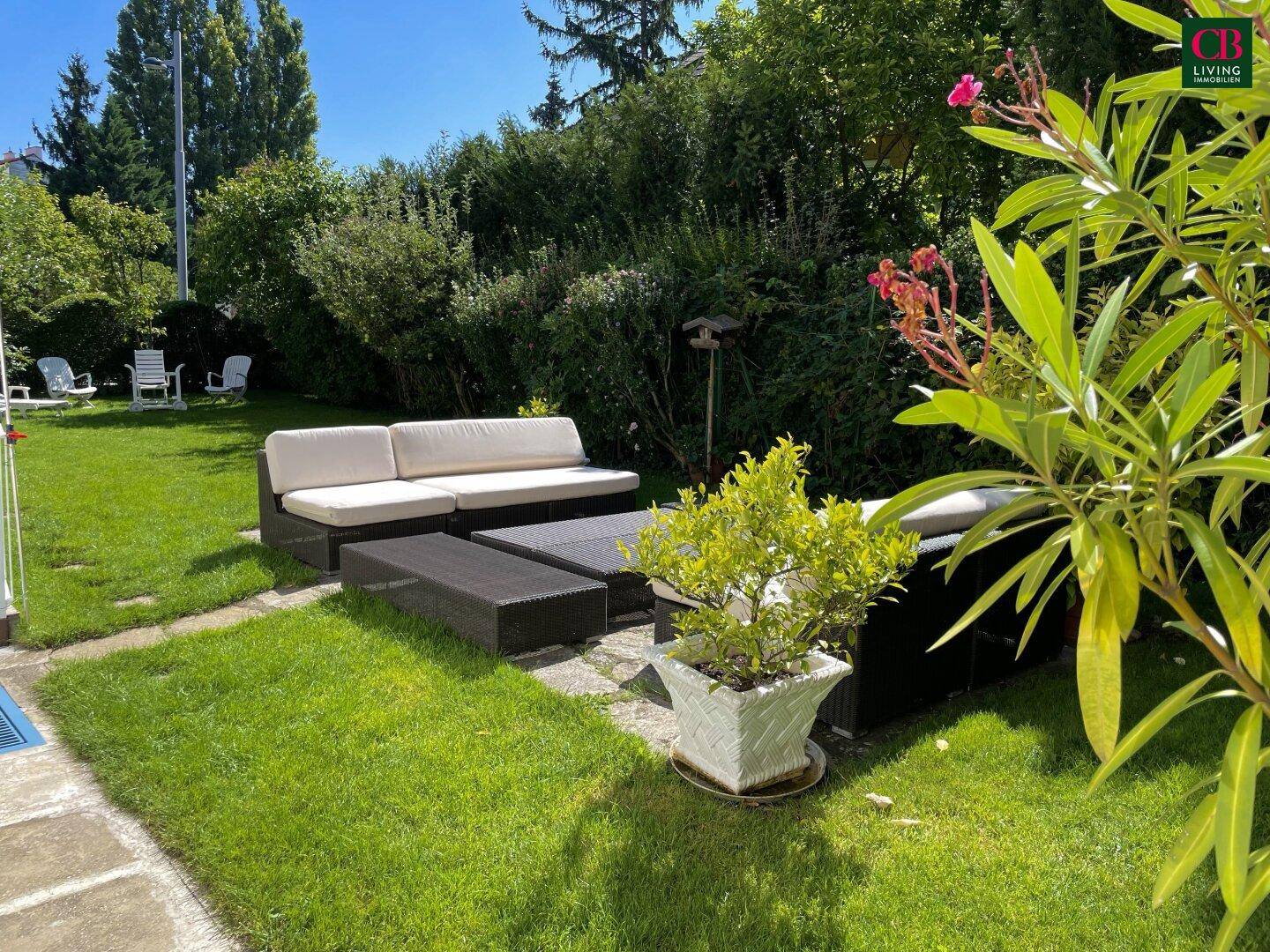 Sonniger Gartenbereich mit bequemen Outdoor-Möbeln und üppiger grüner Bepflanzung.