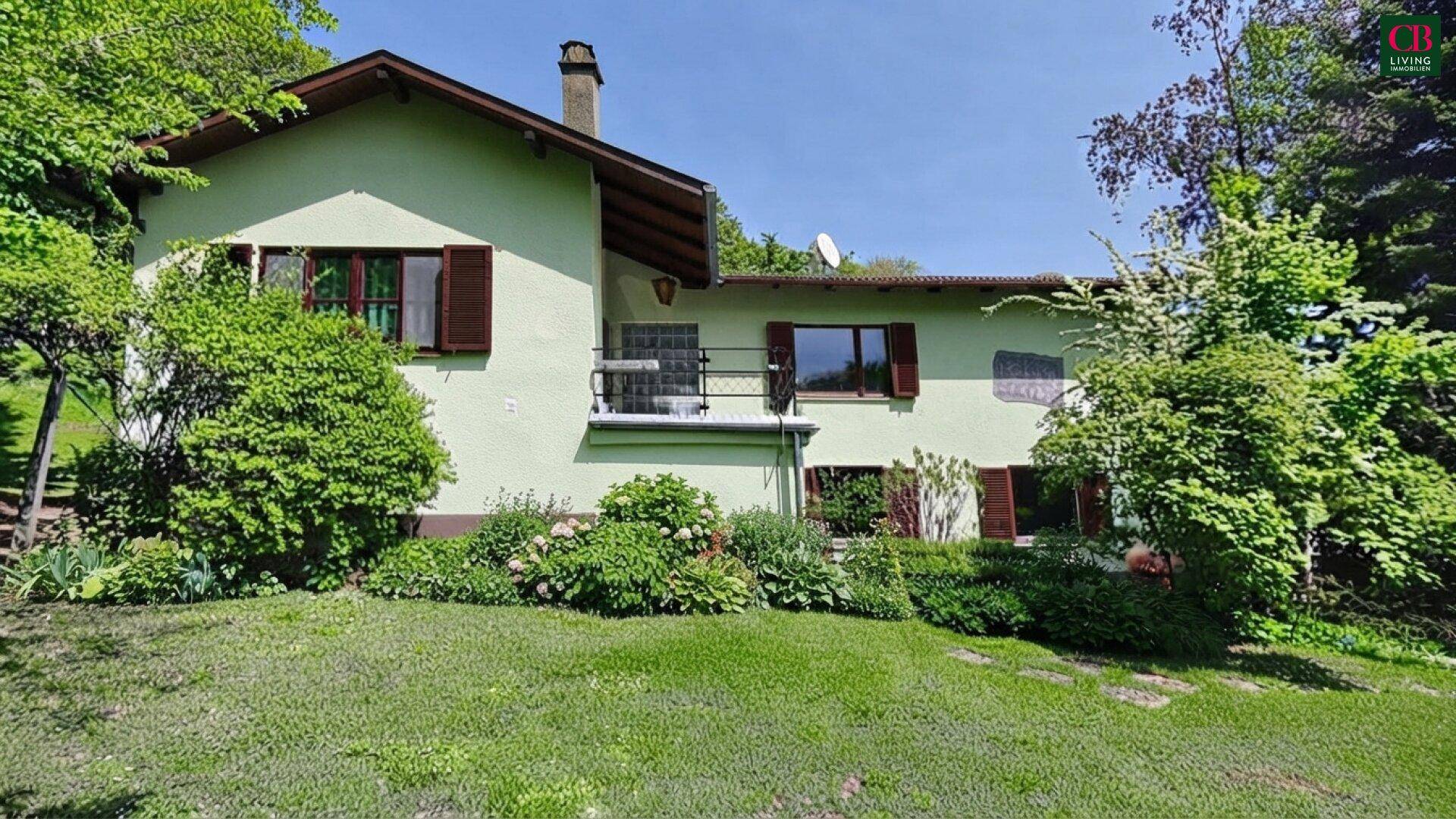 Hausfassade mit Garten und üppiger Vegetation unter blauem Himmel.