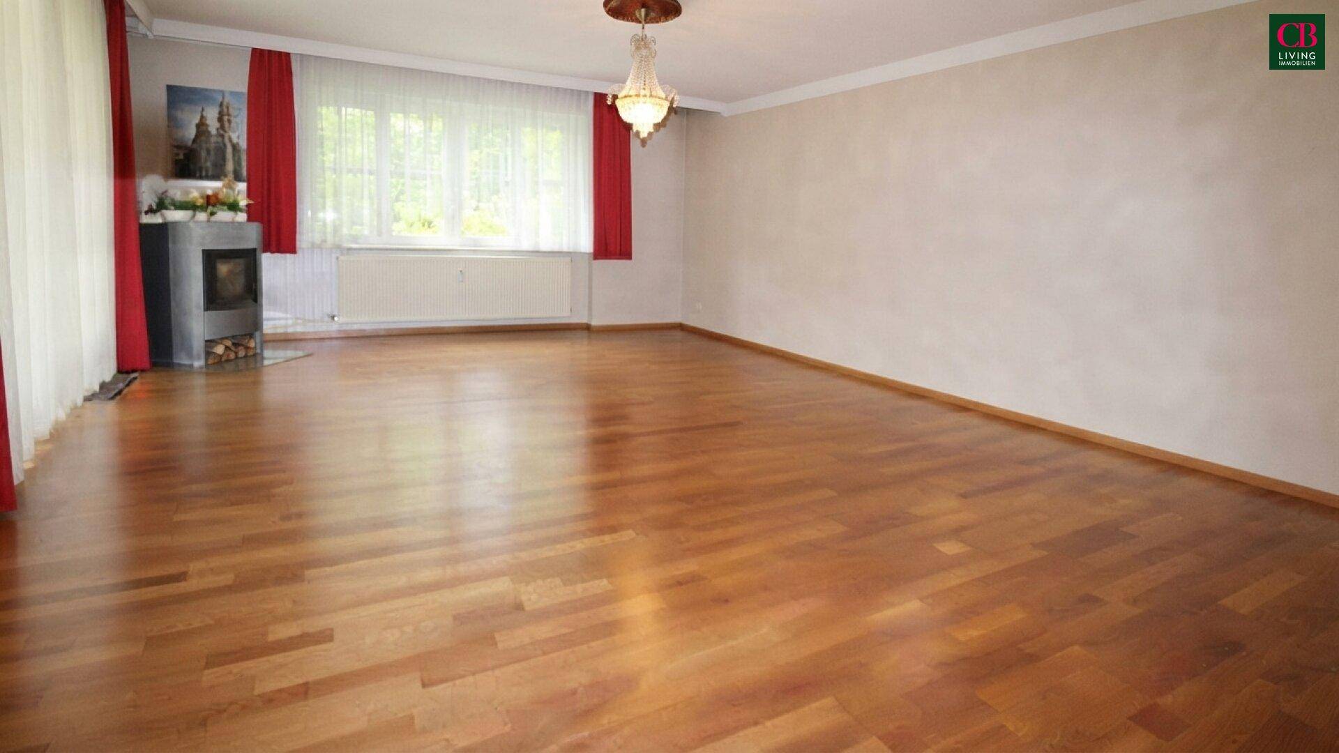 Helles Wohnzimmer mit Parkettboden, Kaminofen und großen Fenstern.