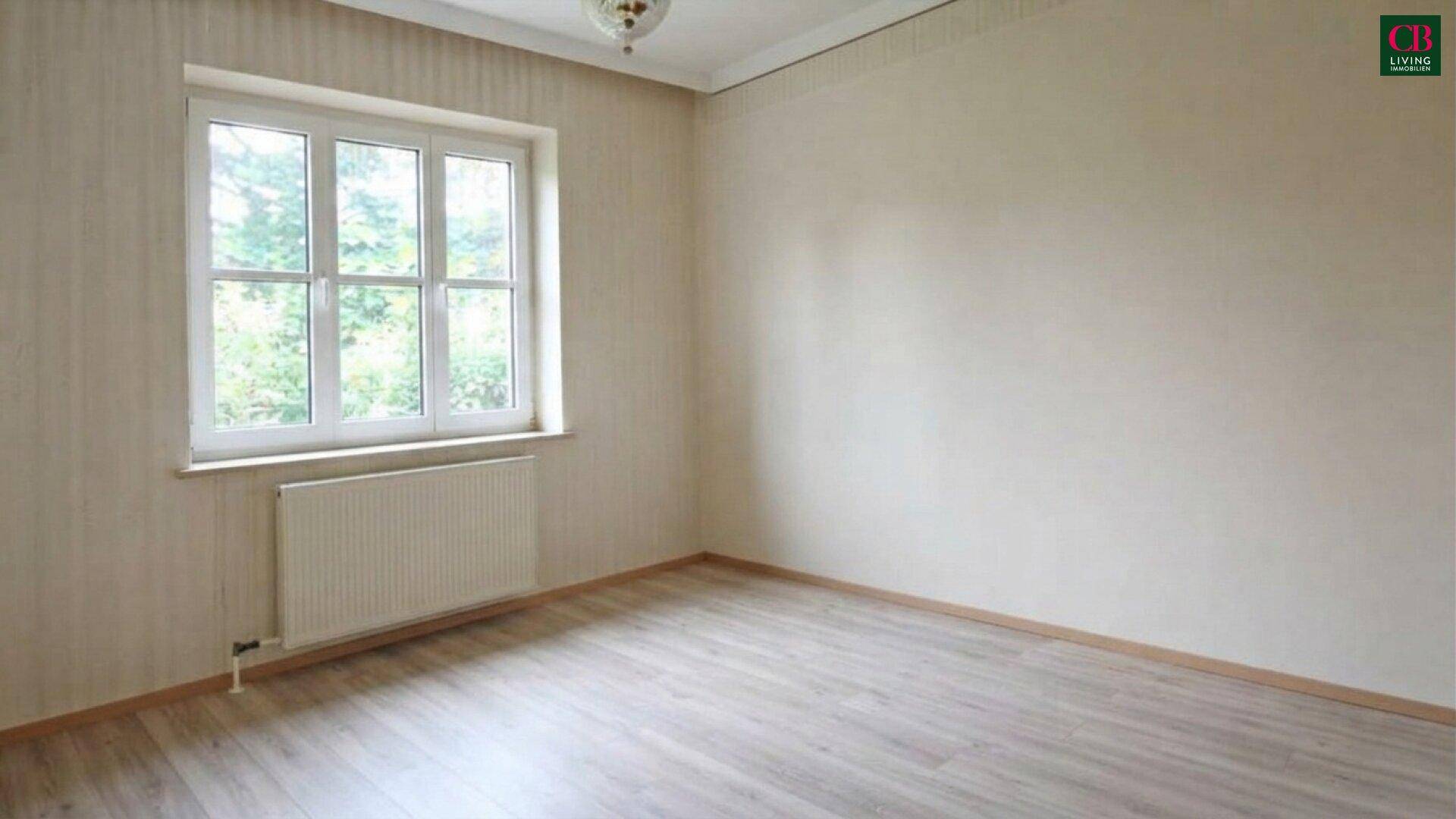 Helles Schlafzimmer mit Laminatboden und großem Fenster mit Blick ins Grüne.