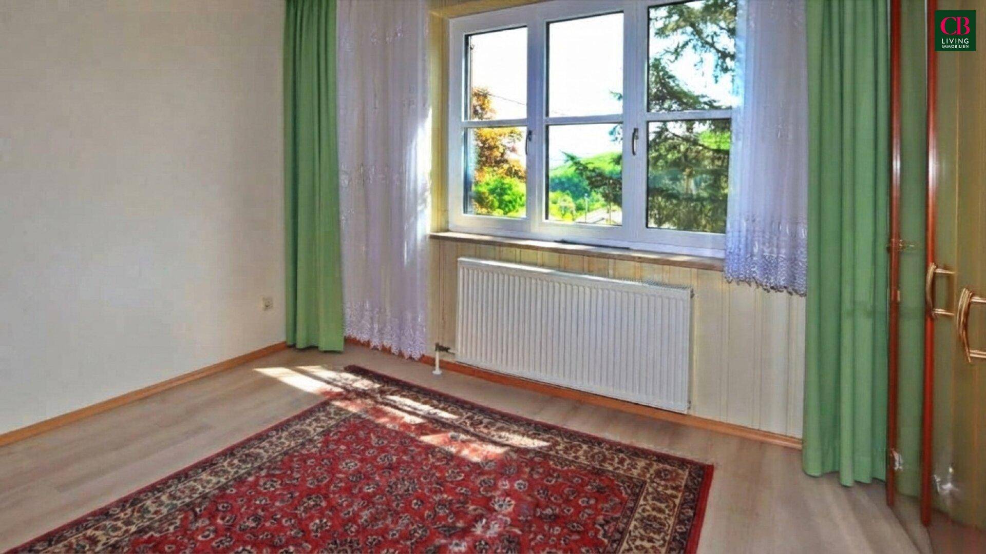 Schlafzimmer mit Laminatboden, grünen Vorhängen und Blick in den Garten.