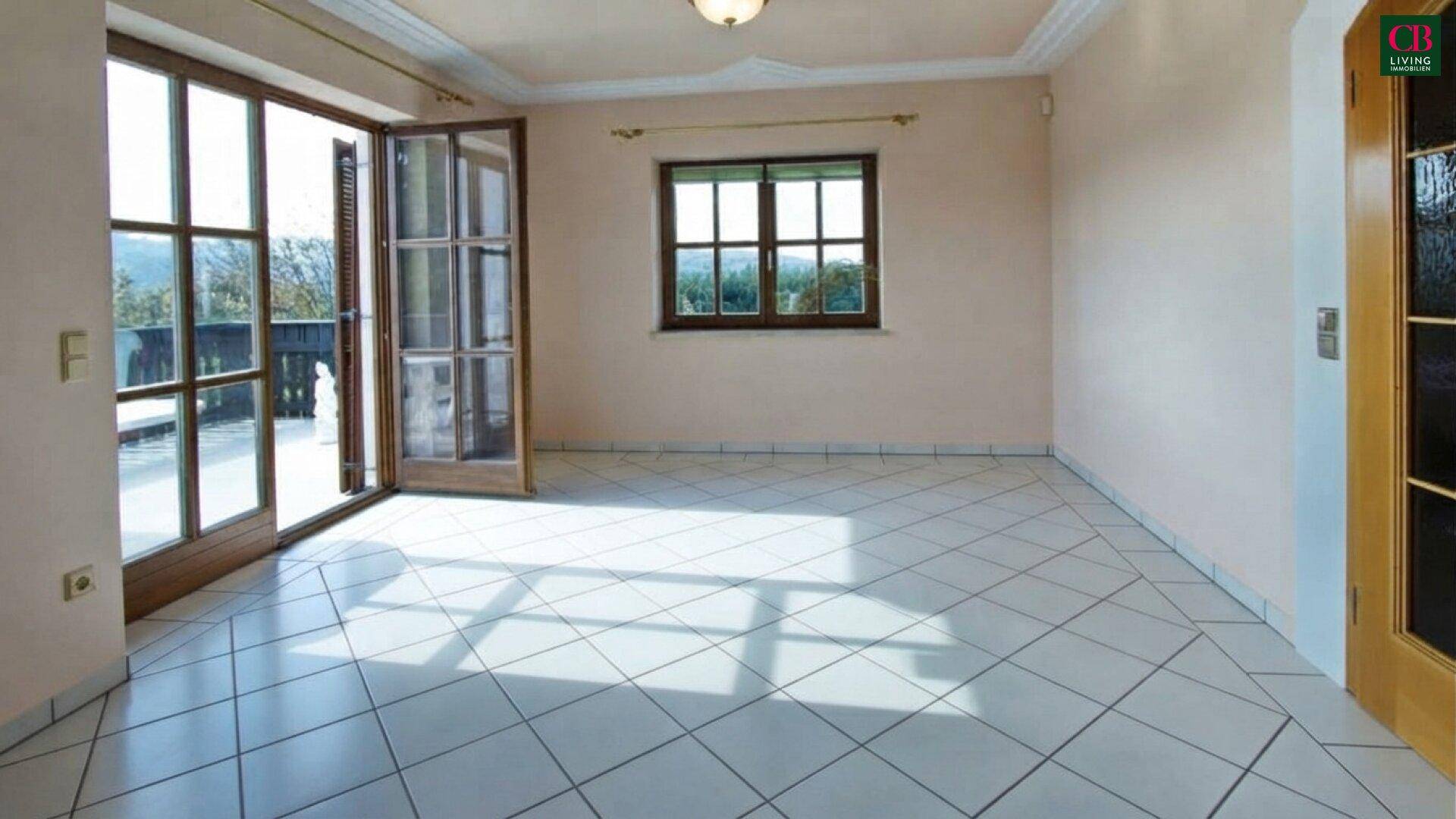 Lichtdurchfluteter Wohnraum mit Fliesenboden und Zugang zu einem Balkon oder einer Terrasse.