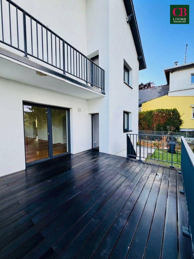 Weitläufige Holzterrasse mit Blick auf den Garten und direkten Zugang zum hellen Innenbereich des Hauses.