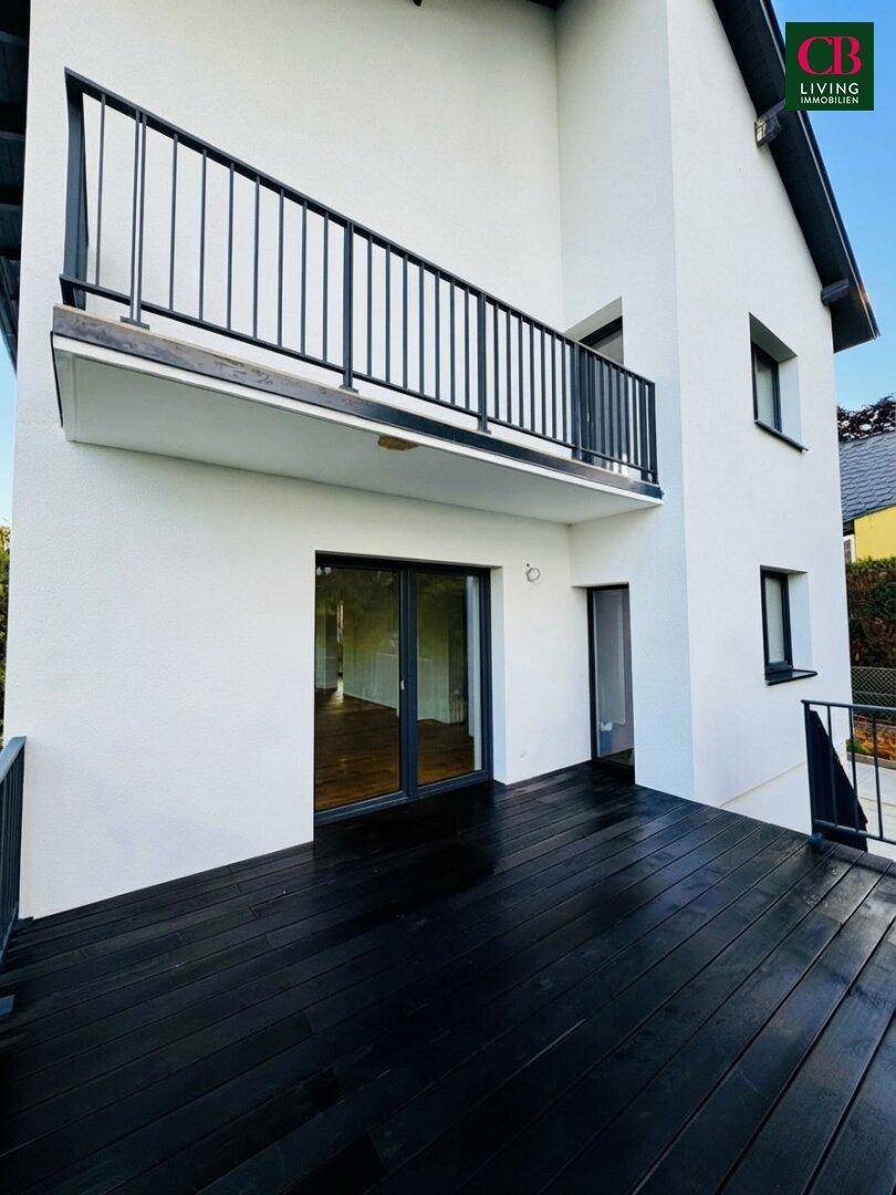 Geräumige Terrasse mit dunklem Holzdeck und Zugang zum Innenbereich durch eine große Glasschiebetür.