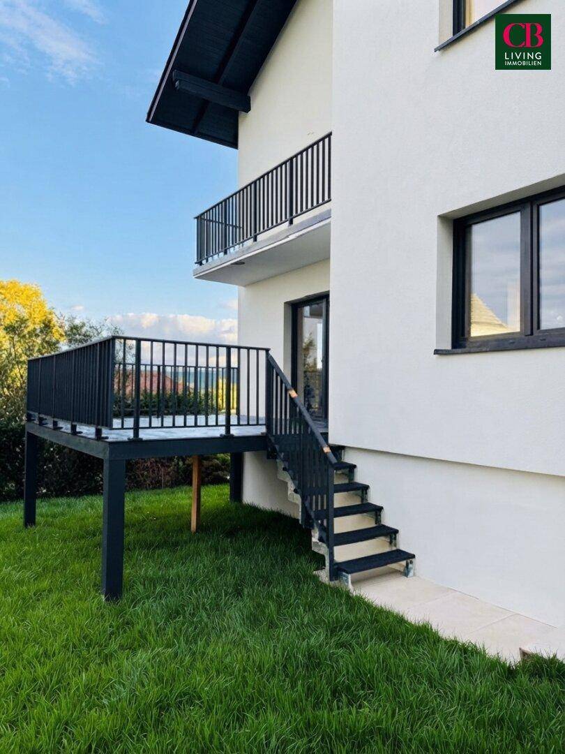 Erhöhte Terrasse mit schwarzem Holzdeck und Treppe zum grünen Rasenbereich des Hauses.