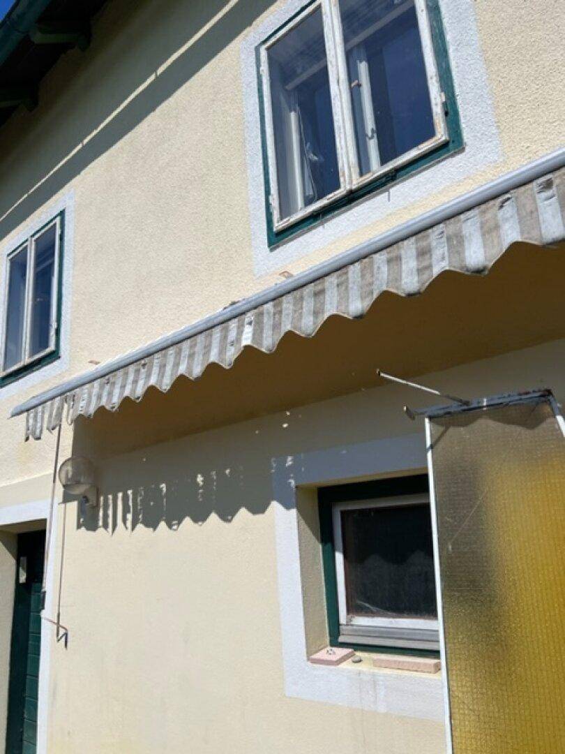 Gelbe Hausfassade mit Fenstern und einer gestreiften Markise unter blauem Himmel.