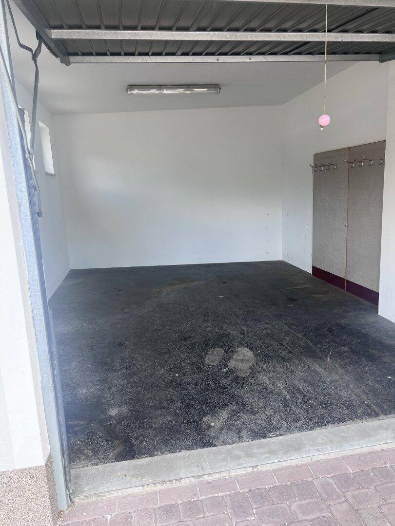 Leere Garage mit Betonboden und einem Rolltor, das den Zugang zum Innenraum ermöglicht.