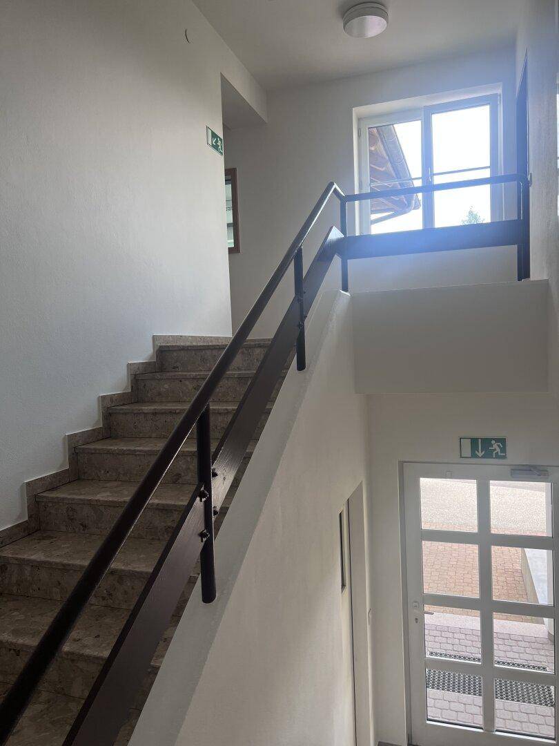Heller Treppenaufgang mit Marmorstufen und einem Fenster, das den Blick nach draußen freigibt.