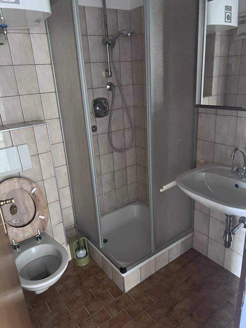 Kleines Badezimmer mit Duschkabine, WC und Waschbecken, gefliest in beigen Farbtönen.