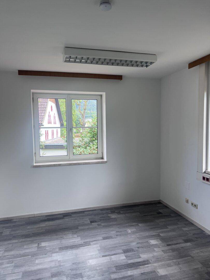 Heller Büroraum mit grauem Laminatboden und einem Fenster, das den Blick ins Grüne ermöglicht.