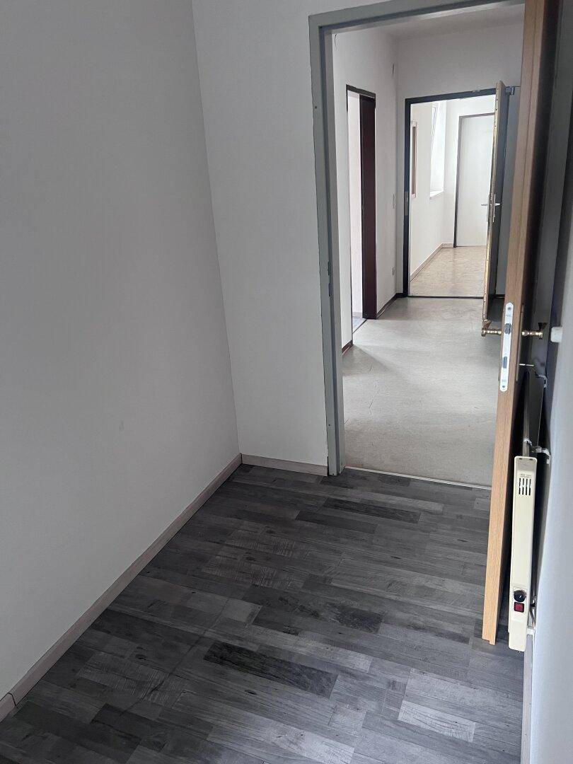 Langer Flur mit grauem Laminatboden und mehreren Türen, die zu verschiedenen Räumen führen.