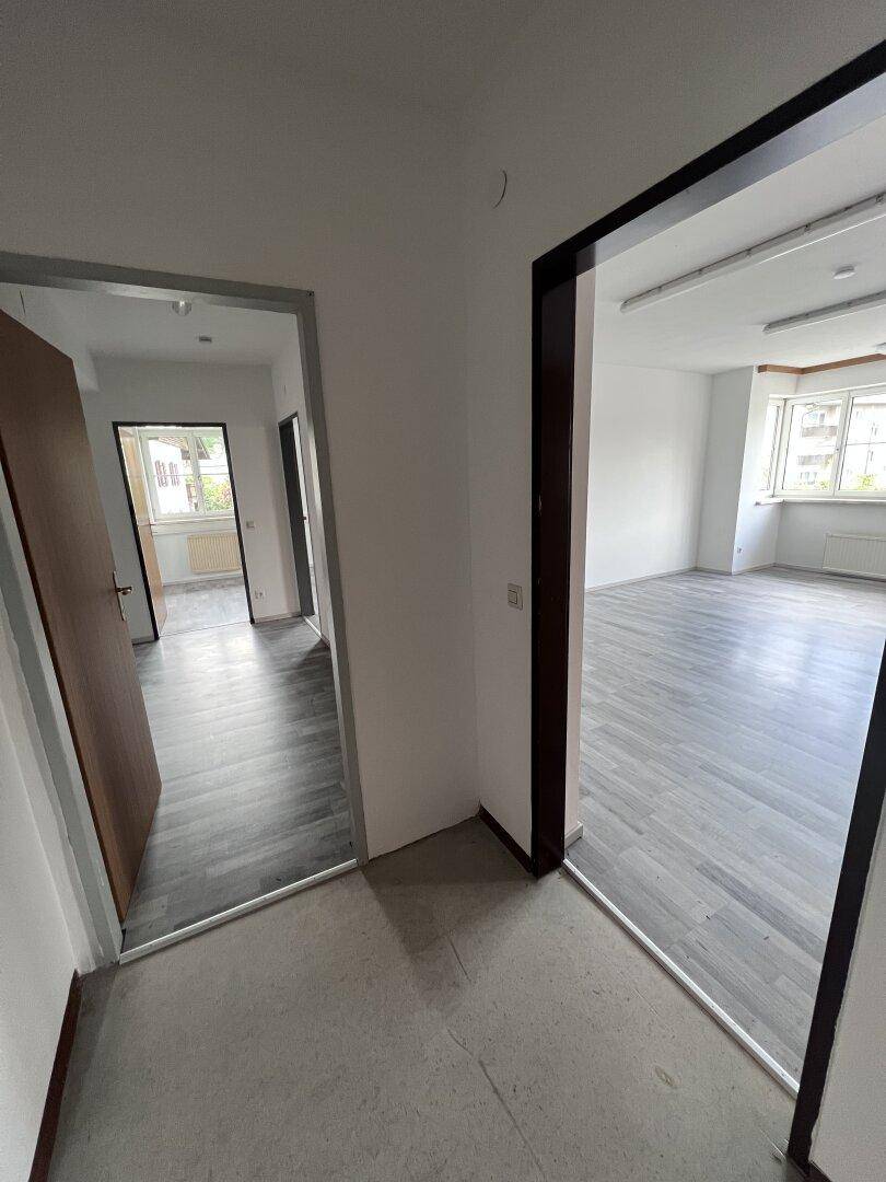 Flur mit Blick in angrenzende Räume, alle mit grauem Laminatboden ausgestattet.