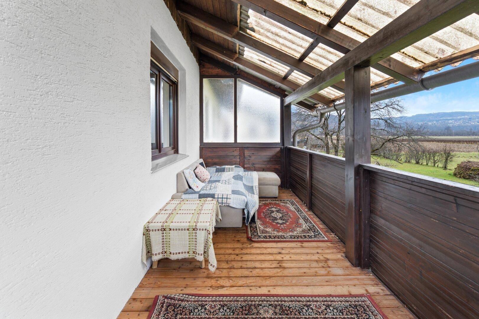 Überdachter Balkon mit Holzboden, Sitzgelegenheiten und weitem Blick in die Landschaft.