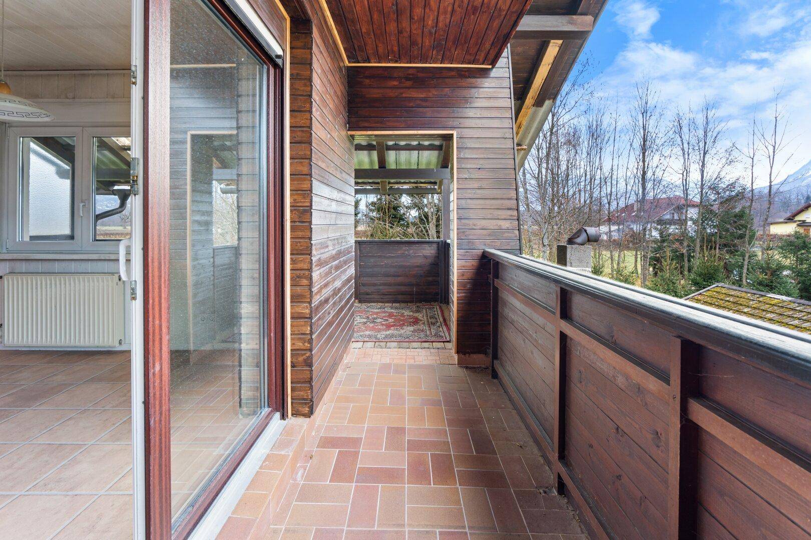 Überdachter Balkon mit Fliesenboden und Holzgeländer, bietet einen schönen Ausblick.