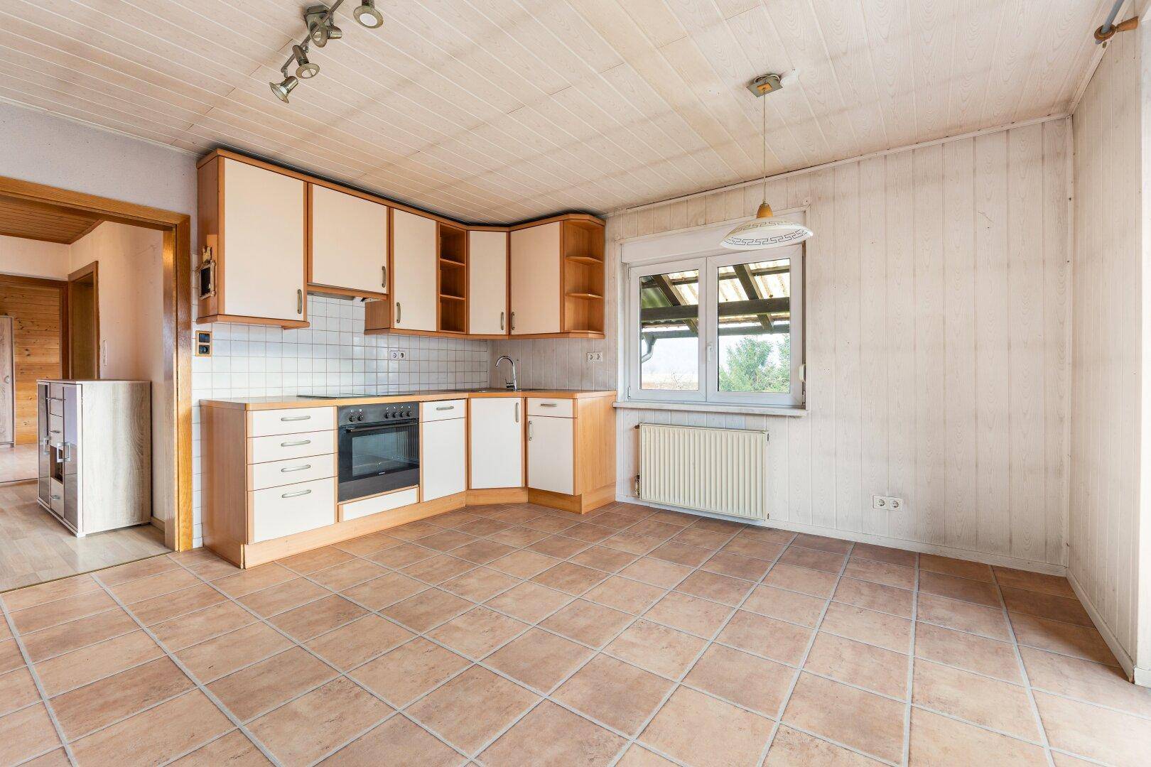 Geräumige Küche mit Einbauküche, Fliesenboden und Blick ins Grüne durch das Fenster.