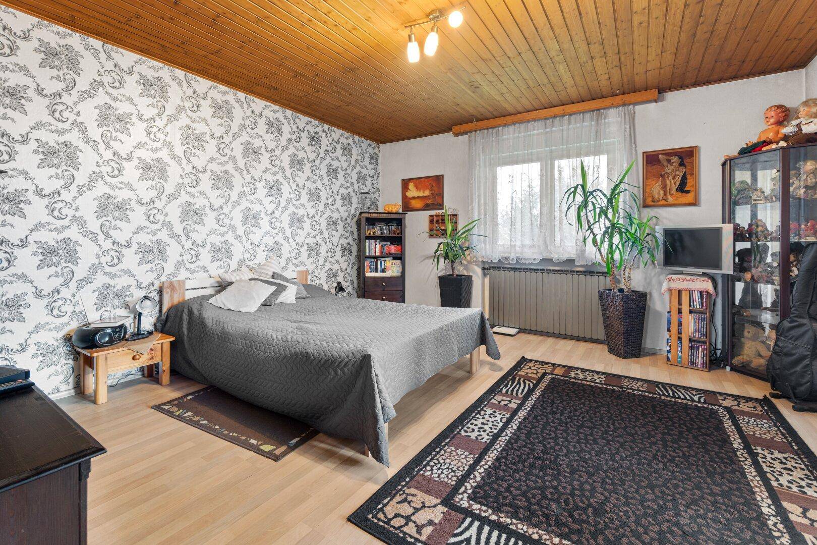 Schlafzimmer mit gemusterter Tapete, Holzdecke und Laminatboden, hell und geräumig.