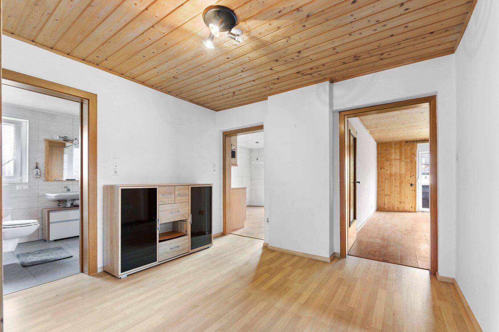Heller Raum mit Laminatboden, weißen Wänden und Holzdecke, mit Zugang zum Badezimmer.