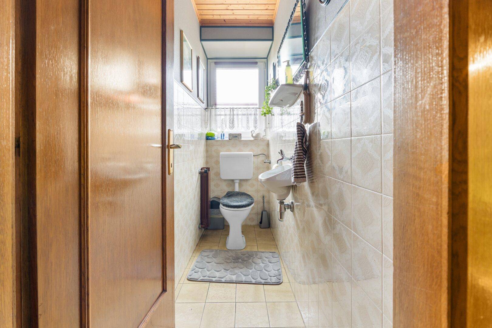 Kleines Gäste-WC mit Toilette, Waschbecken und Fenster, hell gefliest.