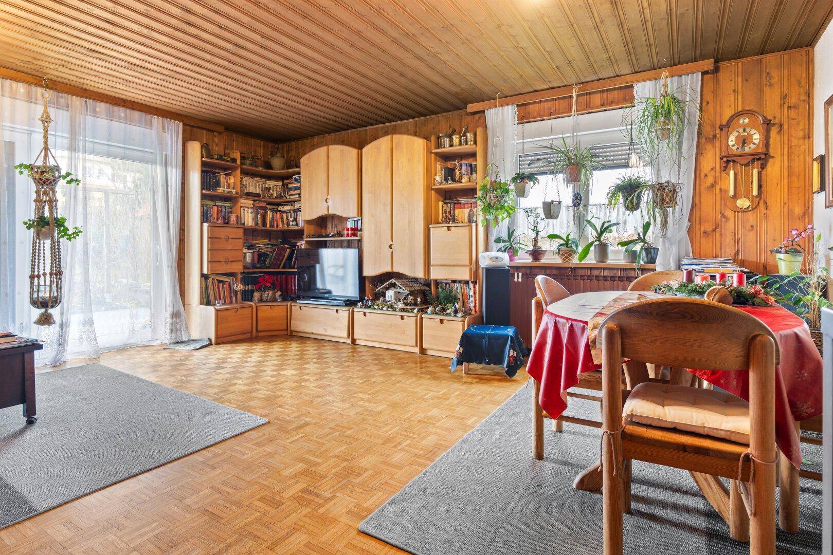 Geräumiges Wohnzimmer mit Parkettboden, Holzdecke und großen Fenstern für viel Licht.