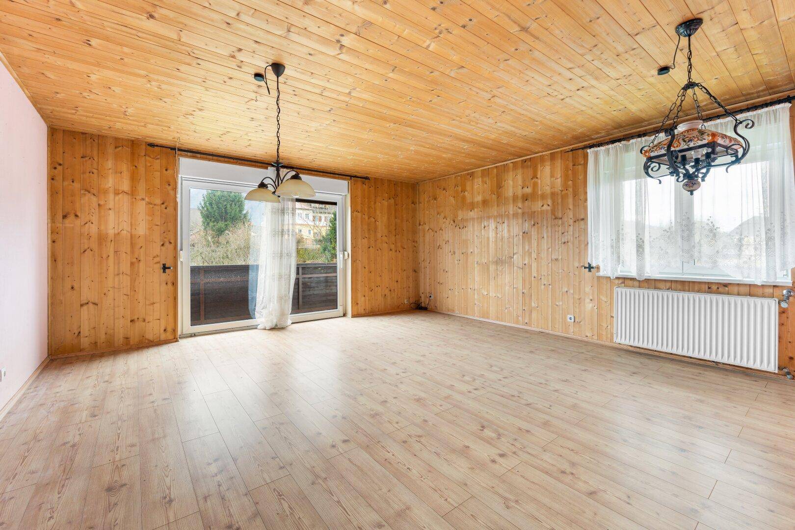 Helles Wohnzimmer mit Holzvertäfelung, Laminatboden und Zugang zum Balkon.