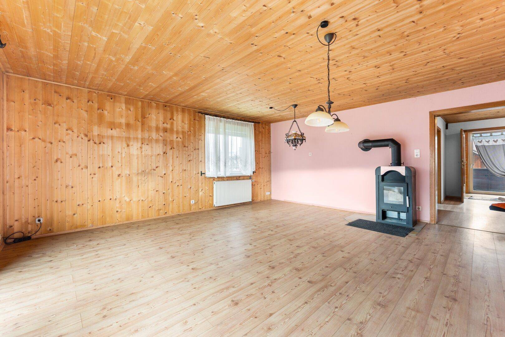 Geräumiger Wohnraum mit Laminatboden, Holzvertäfelung und einem modernen Holzofen.