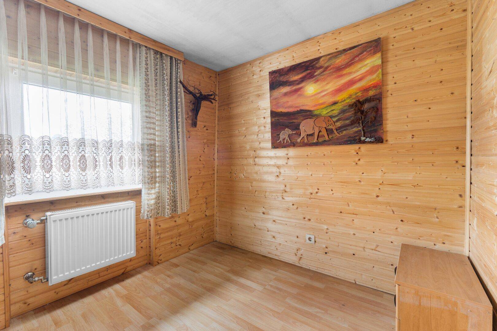 Gemütlicher Raum mit Holzvertäfelung, Laminatboden und Fenster, ideal als Gästezimmer.