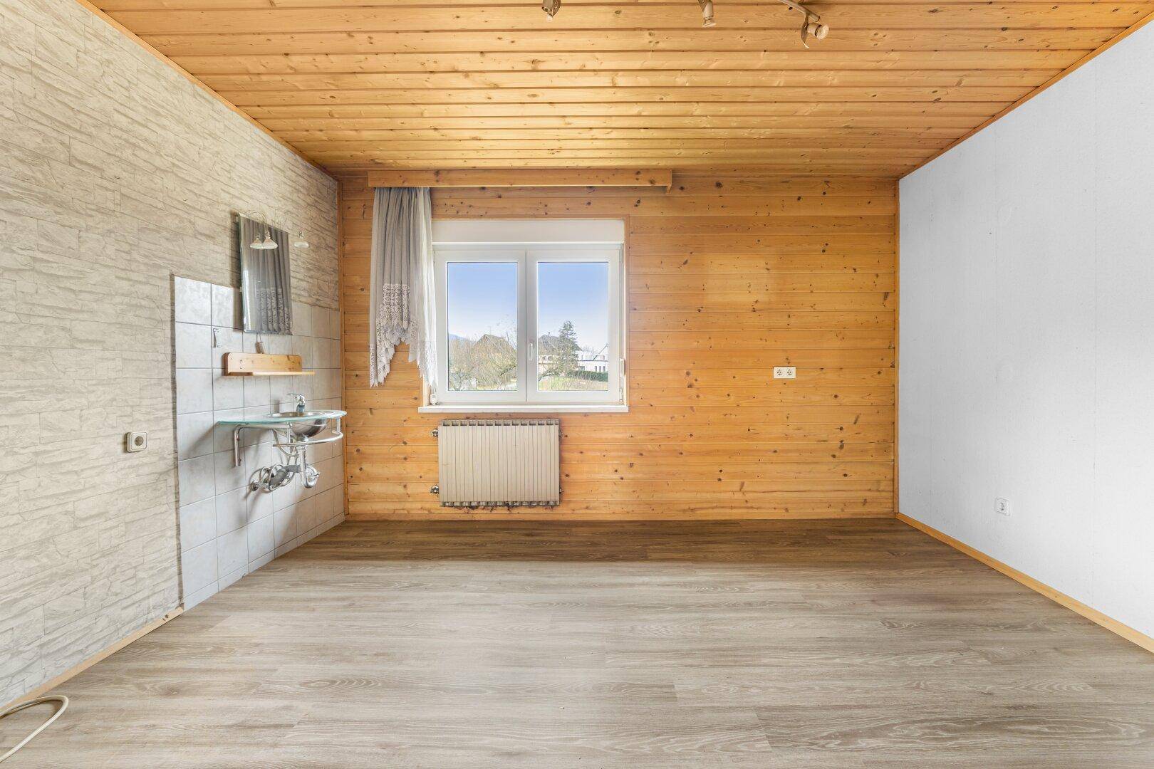 Raum mit Laminatboden, Holzdecke und kleinem Waschbeckenbereich an der Wand.