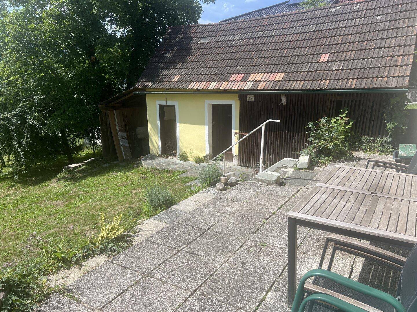Gemütlicher Terrassenbereich mit Holztisch und Stühlen neben einem Nebengebäude.