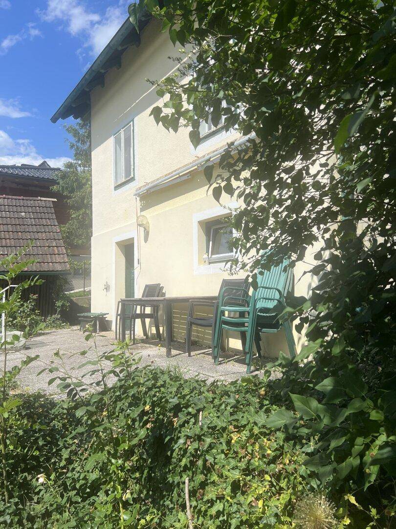 Kleiner Terrassenbereich am Haus mit einfachen Gartenmöbeln und umgebendem Grün.