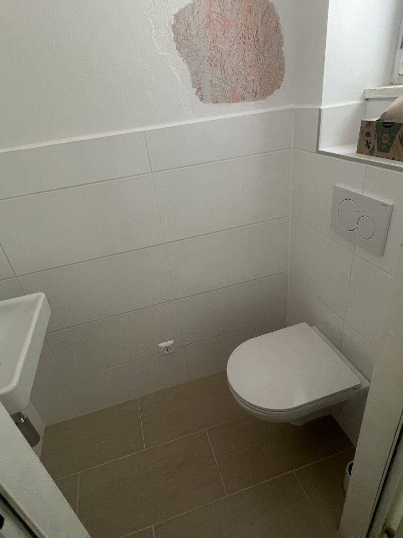 Modernes Gäste-WC mit wandhängender Toilette, kleinem Waschbecken und hellen Fliesen.