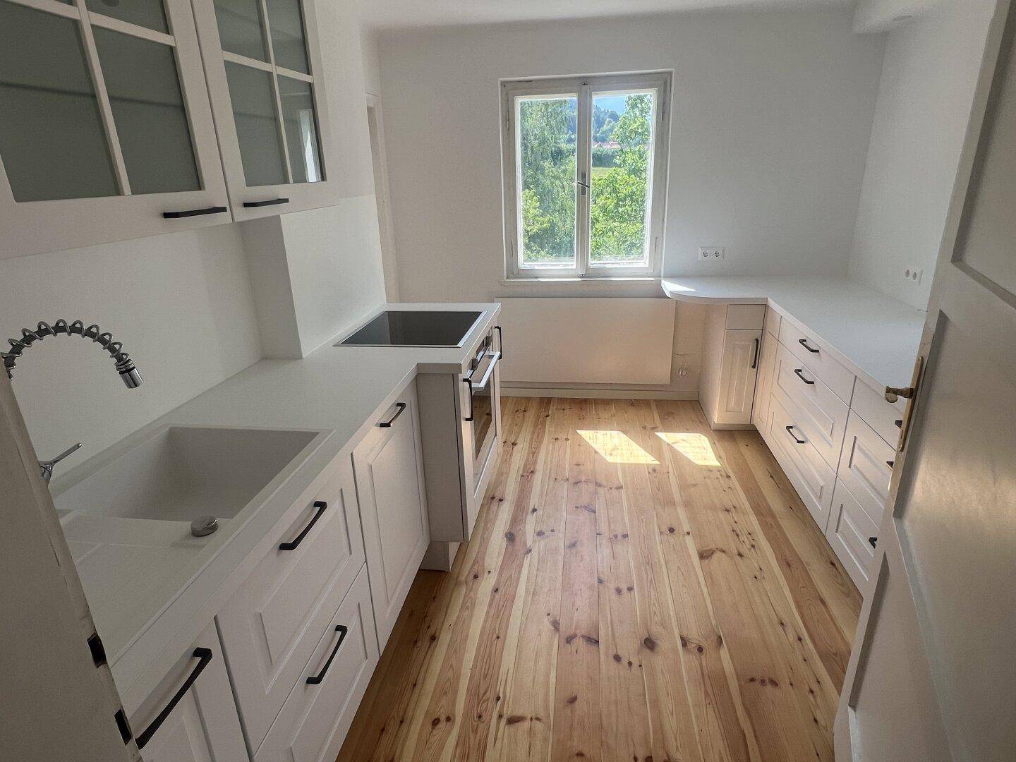 Helle Einbauküche mit weißen Schränken, Spüle, Kochfeld und Holzfußboden.