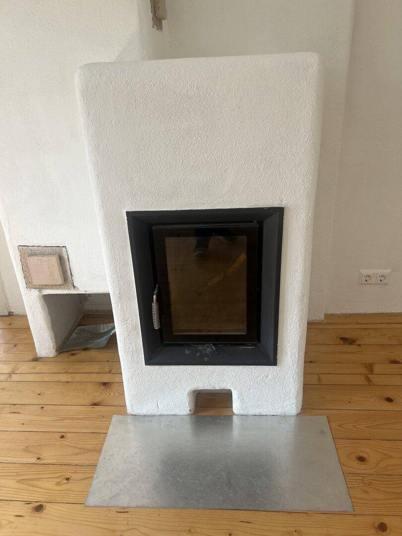 Nahaufnahme eines modernen Kaminofens mit schwarzer Glastür und Holzfach.