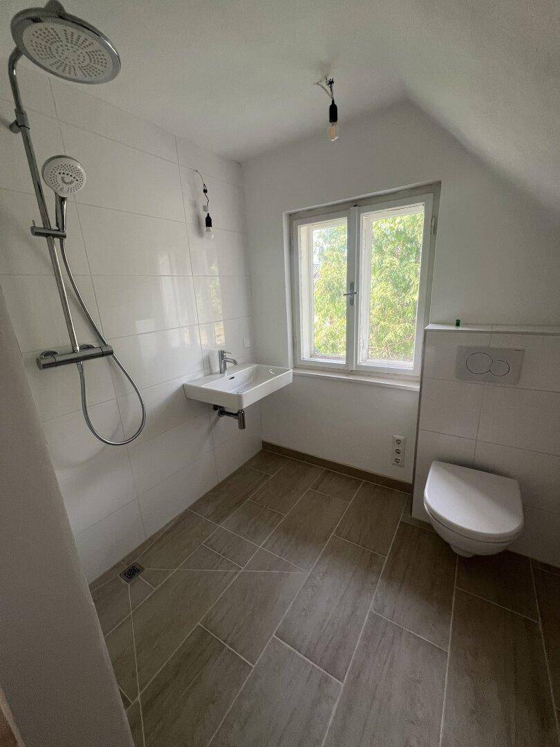 Modernes Badezimmer im Dachgeschoss mit Dusche, Waschbecken, Toilette und Fenster.
