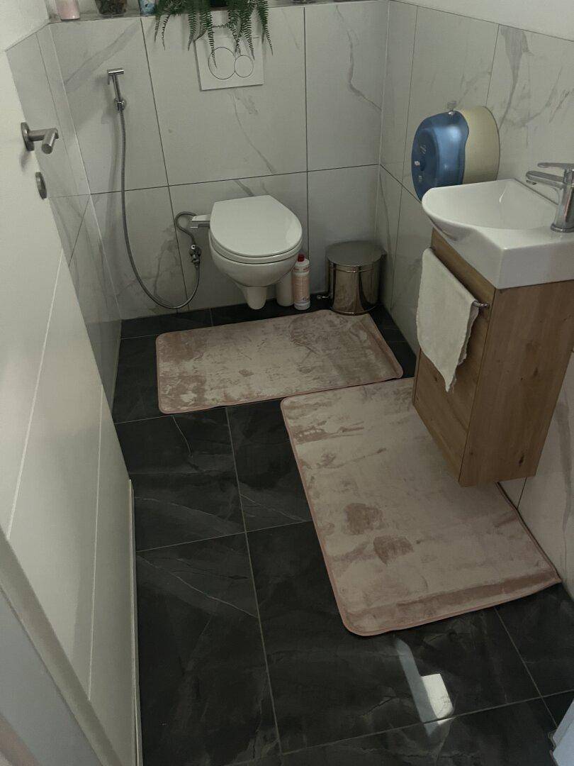 Kleines WC mit wandhängender Toilette, Waschbecken und dunklen Fliesen am Boden und an den Wänden.