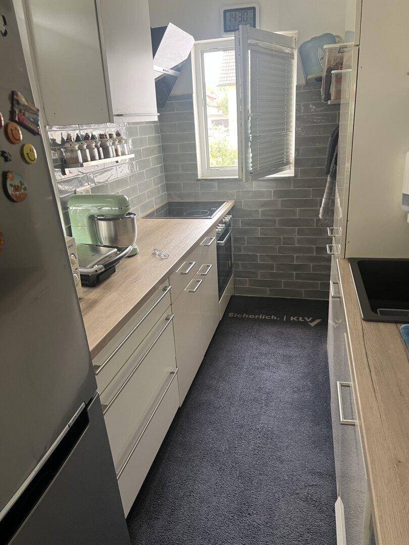 Schmale Küche mit weißen Schränken, Holzarbeitsplatte und grauen Fliesen als Spritzschutz.