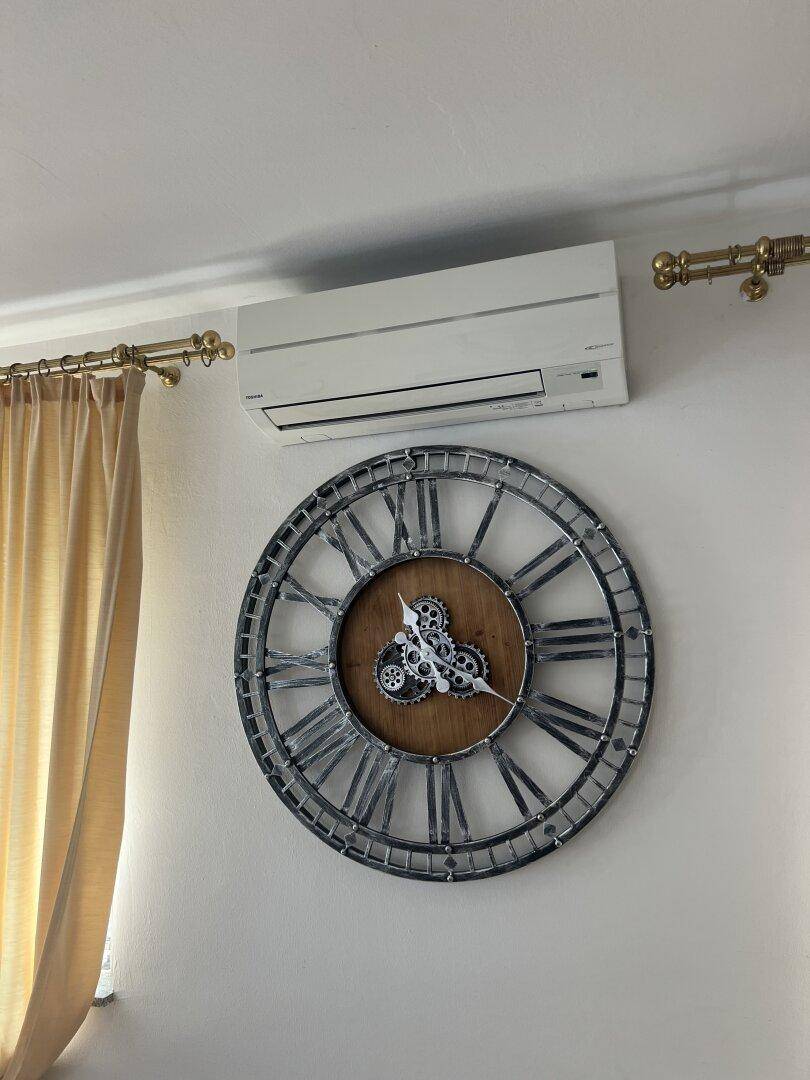 Wandmontierte Klimaanlage über einer großen dekorativen Uhr in einem hellen Raum.