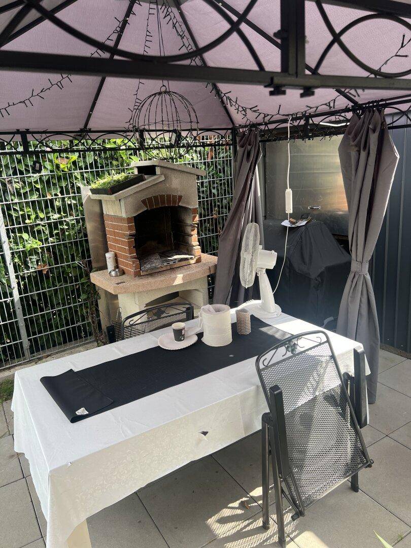 Gemütlicher Außenbereich unter einem Pavillon mit Esstisch und gemauertem Grill.