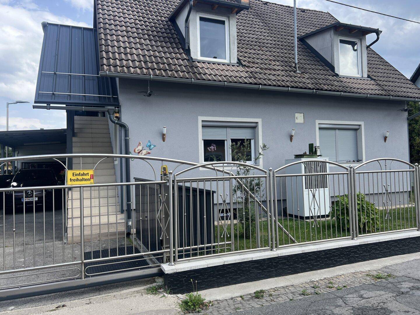 Einfamilienhaus mit grauer Fassade, Satteldach und einem gepflegten Vorgartenbereich.