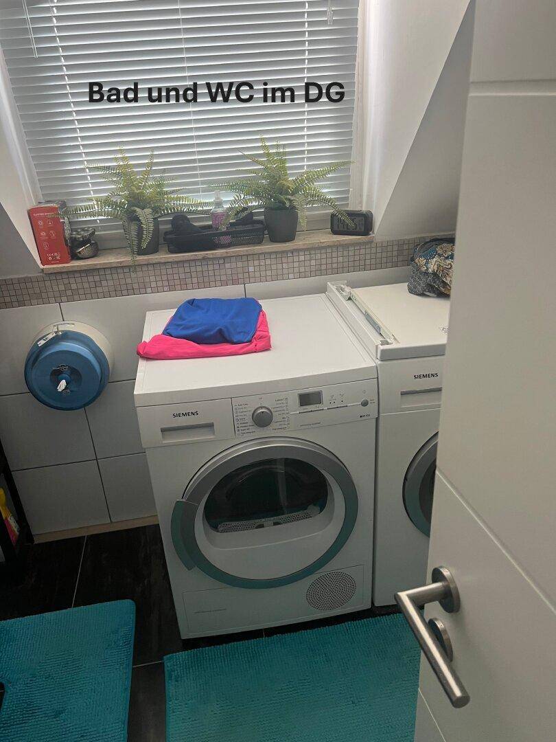 Badezimmer im Dachgeschoss mit Waschmaschine, Trockner und Fenster unter einer Dachschräge.