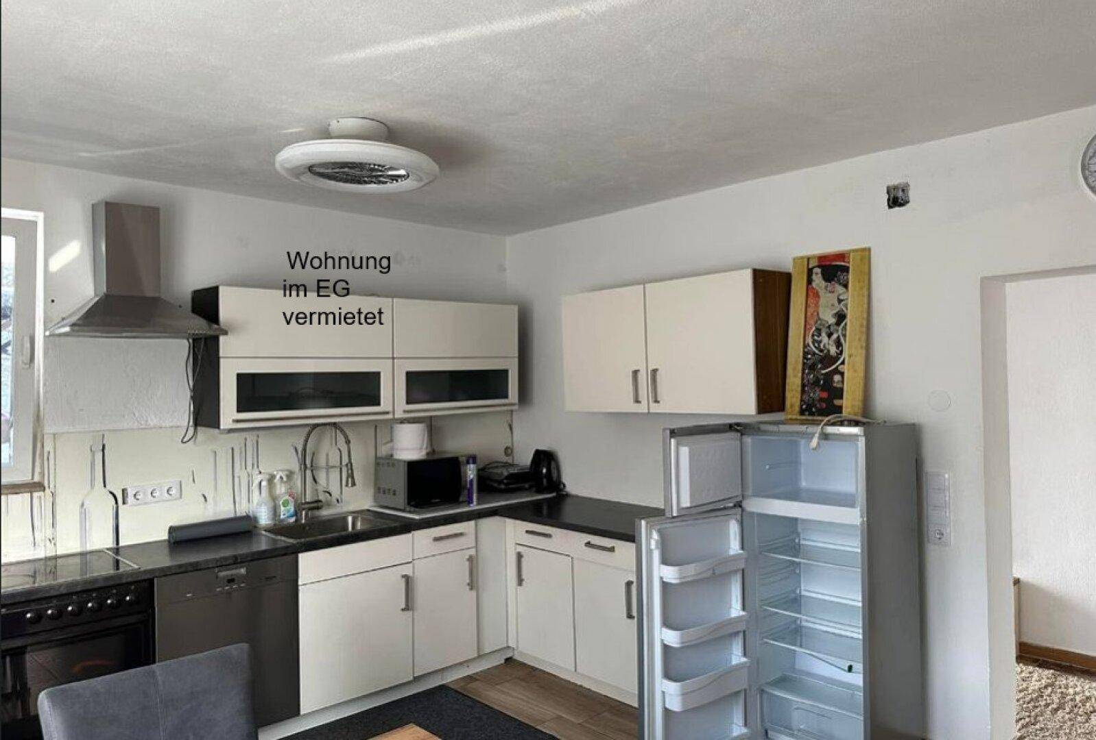 Küche in einer Erdgeschosswohnung mit weißen Schränken, schwarzer Arbeitsplatte und modernen Geräten.