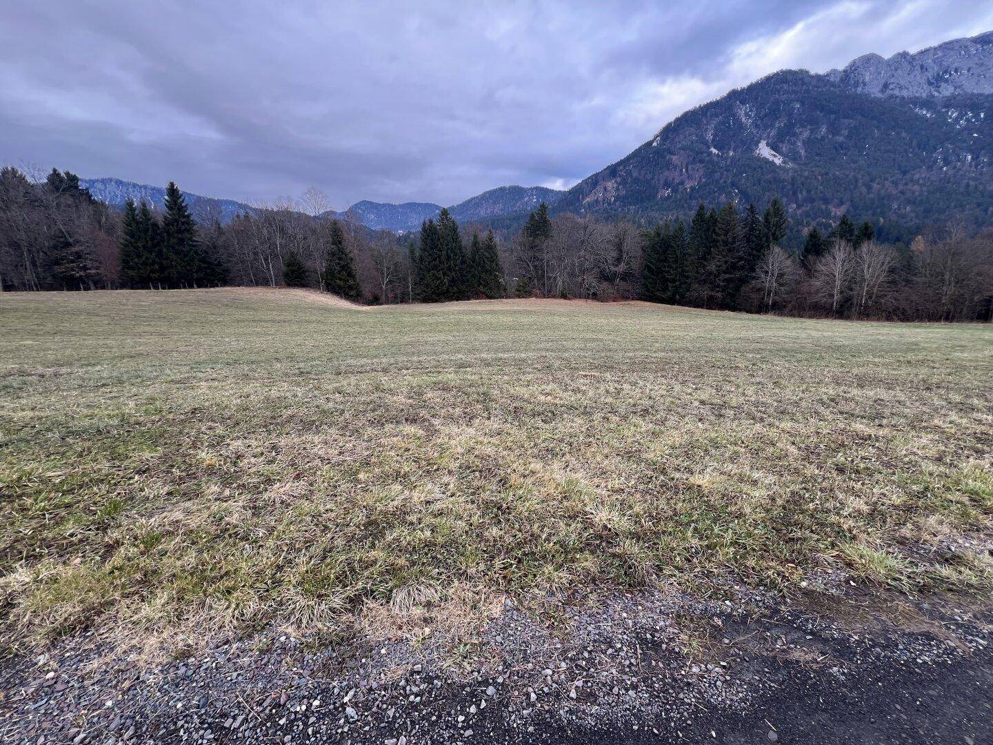 Offenes Feld mit Blick auf die umliegende Berglandschaft unter einem grauen Himmel.