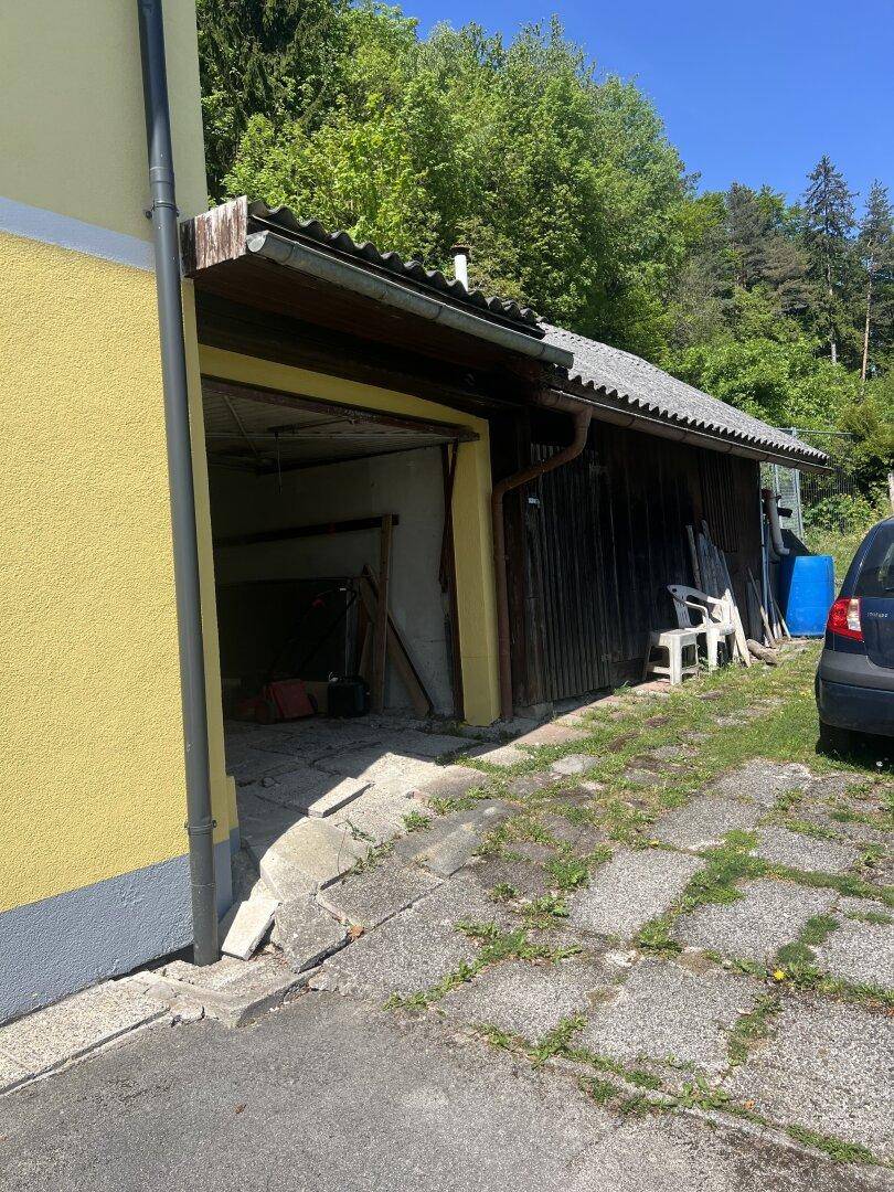Offene Garage neben einem Holzschuppen mit Blick auf die grüne Umgebung.