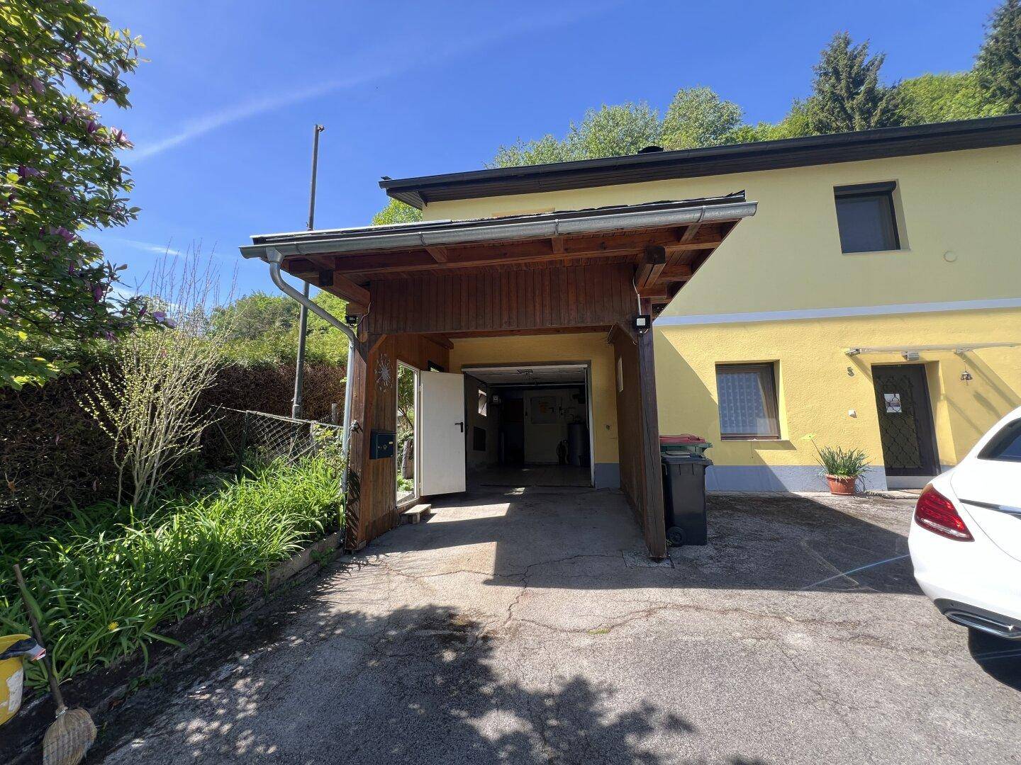 Überdachter Carport vor der Garage eines gelben Wohnhauses mit Auffahrt.